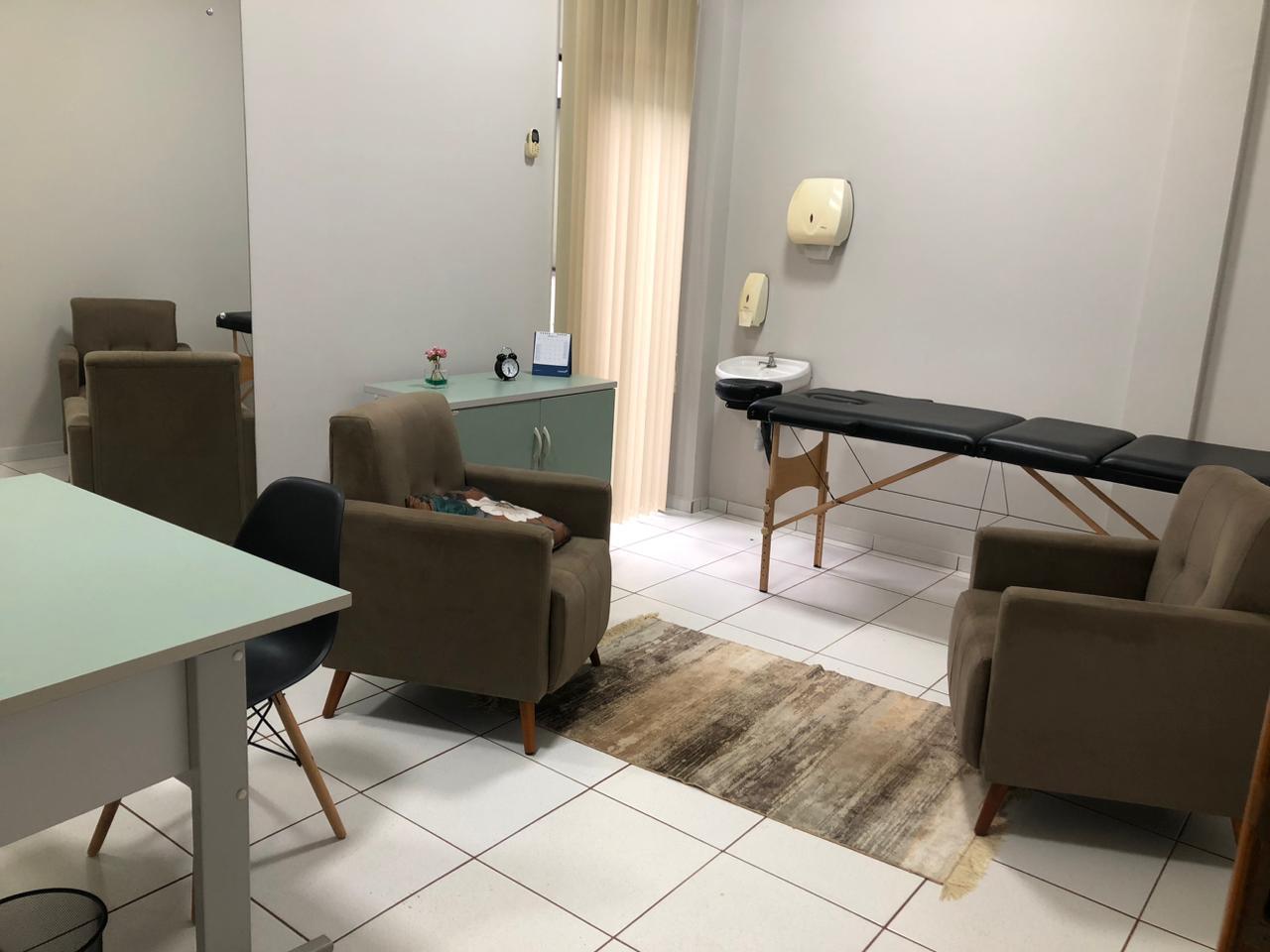 Sala de atendimento com poltronas, mesa de apoio, pia e maca para terapias