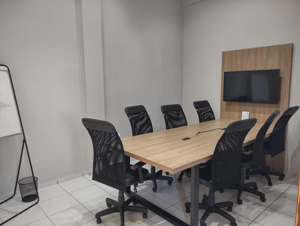Sala de reunião com mesa de madeira, oito cadeiras e TV para apresentações