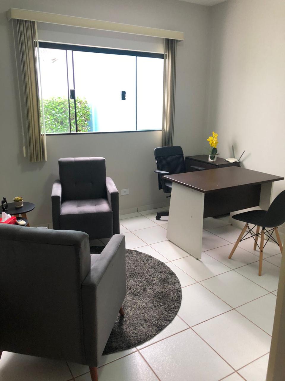 Consultório com poltronas, mesa de trabalho e janela ampla com luz natural